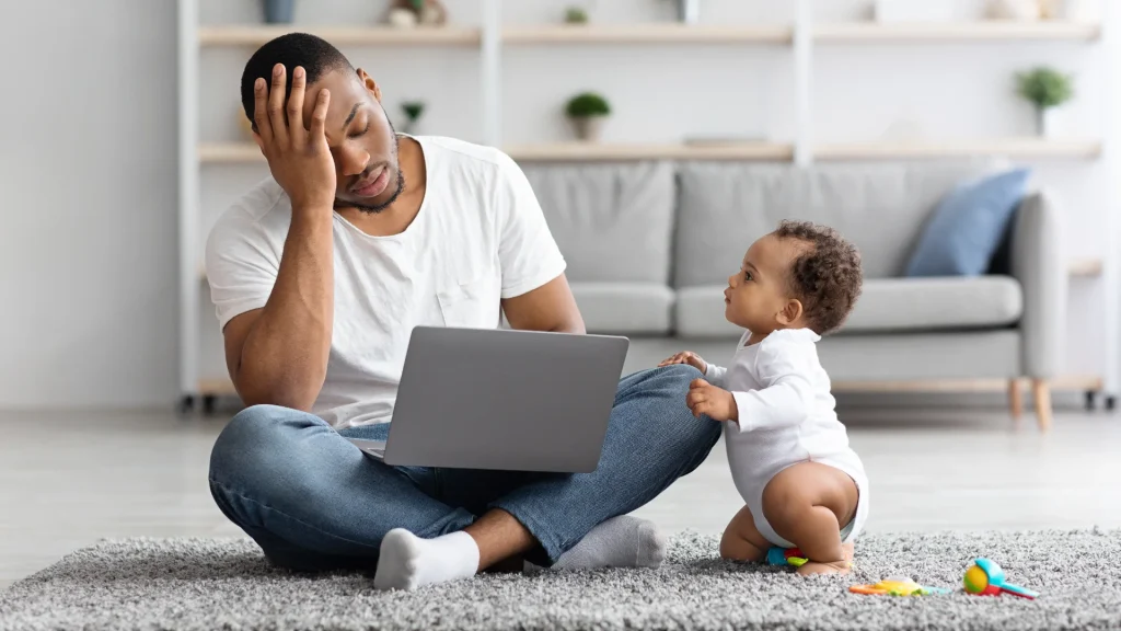 Stressed businessperson juggling a baby and laptop, symbolising high-maintenance websites.